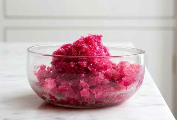 A glass bowl filled with Campari sorbet on a white marble countertop.