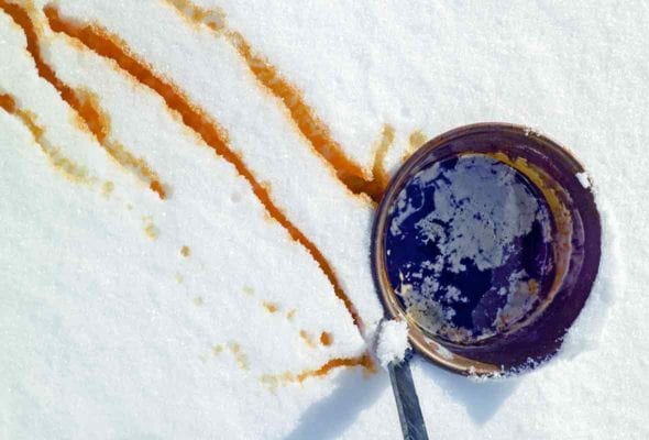 A bucket of maple syrup in the snow with streaks of maple syrup snow nearby