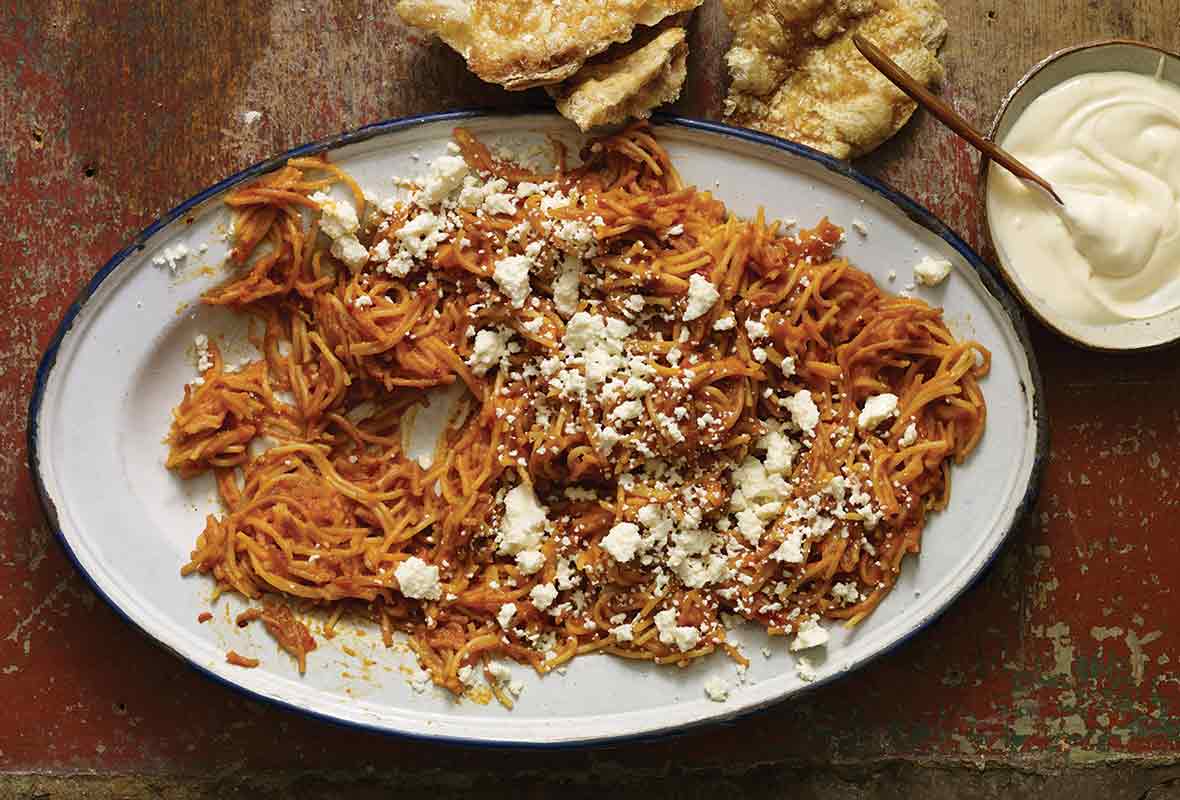 A platter of Mexican spaghetti with a bowl of crema on the side.