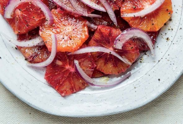 A white plate filled with blood orange and red onion salad with a grinding of pepper on top.