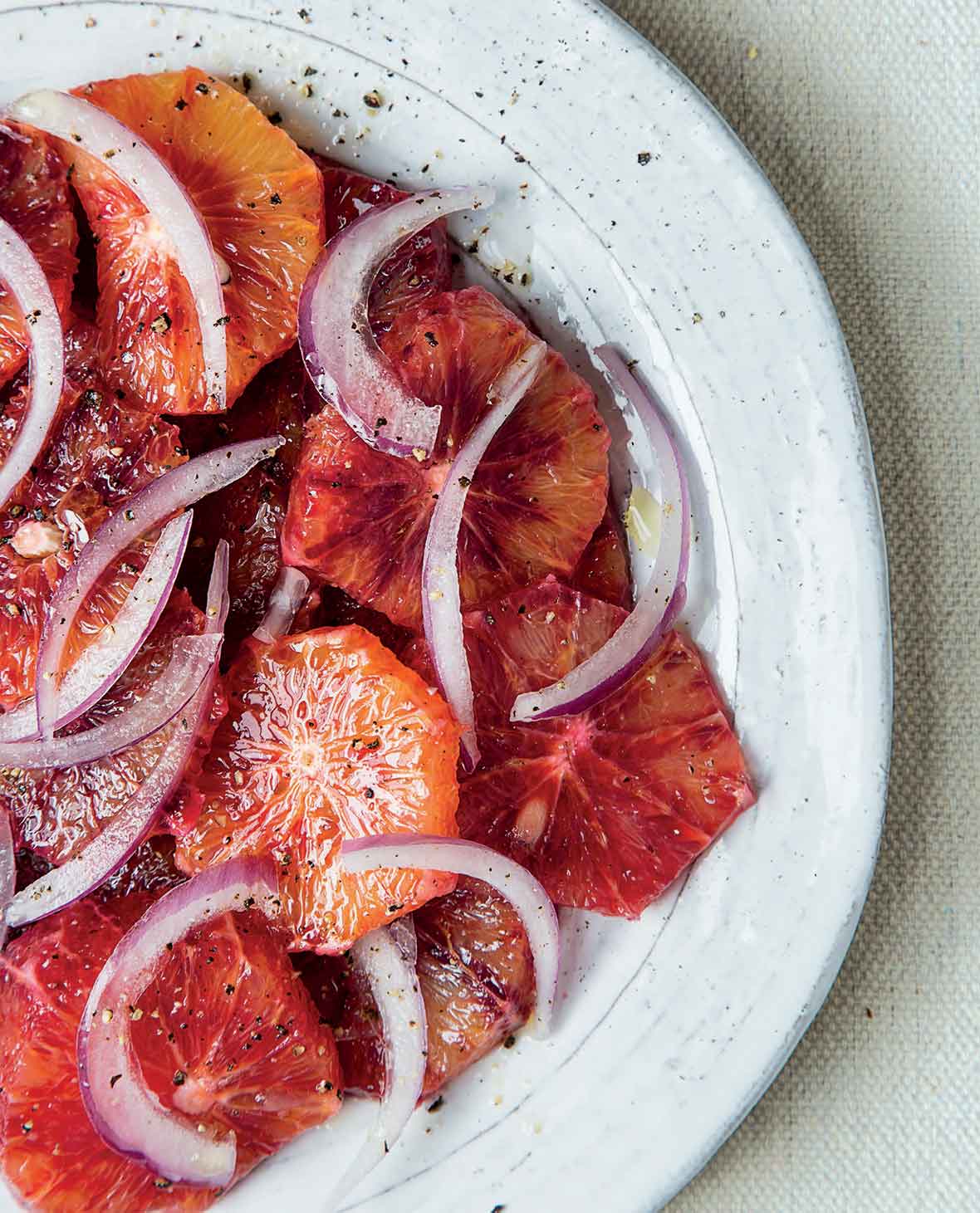 A white plate filled with blood orange and red onion salad with a grinding of pepper on top.