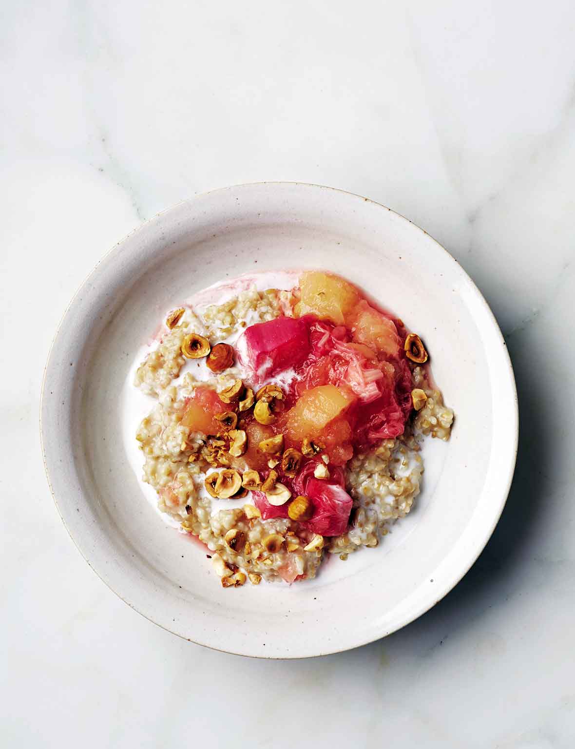A white bowl filled with steel cut oats with rhubarb applesauce and chopped pistachios on top.