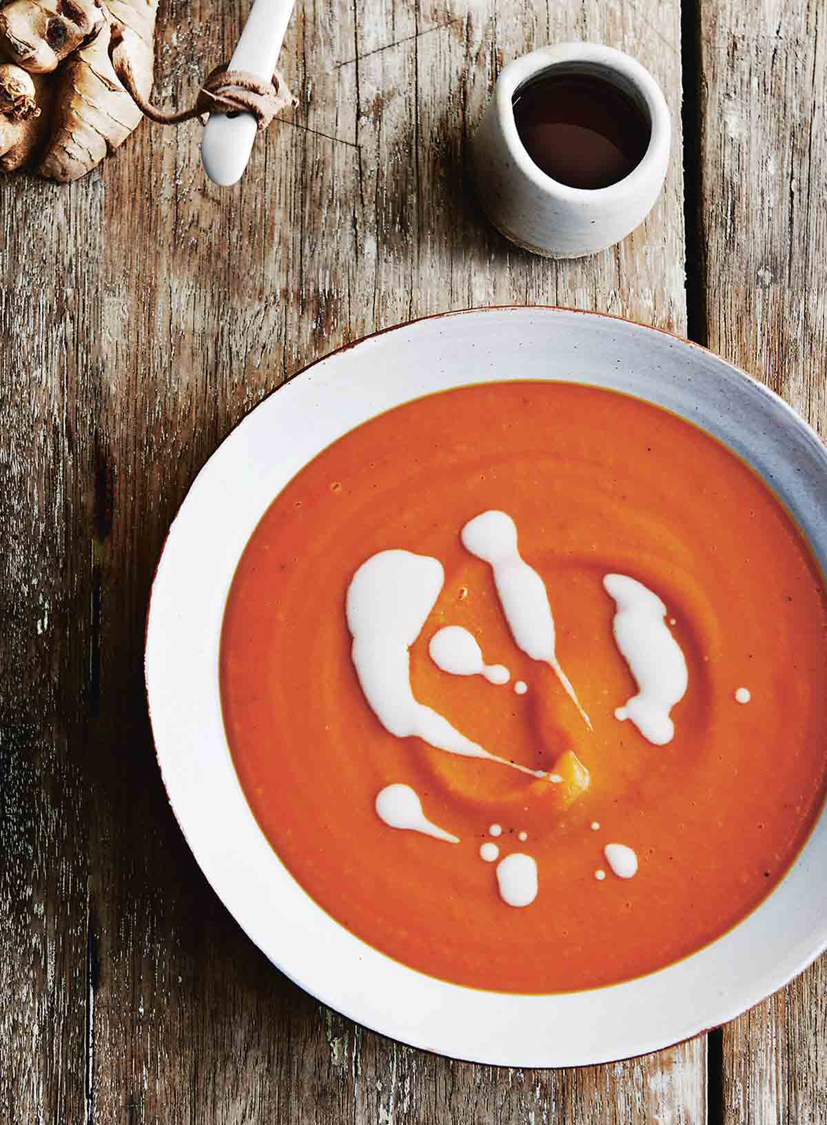 A white earthenware bowl of sweet potato soup with coconut milk drizzled over the top.