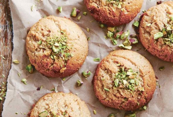 Six tahini cookies on a piece of parchment with chopped pistachios on the cookies and on the parchment.