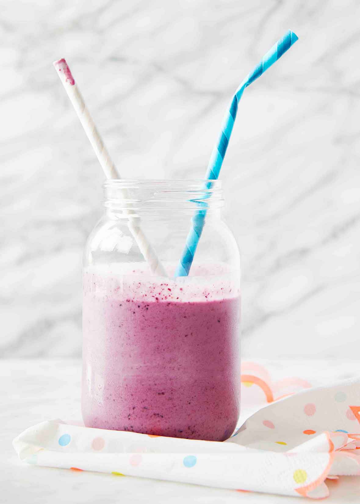 A PB&J smoothie in a mason jar with two striped straws sticking out.