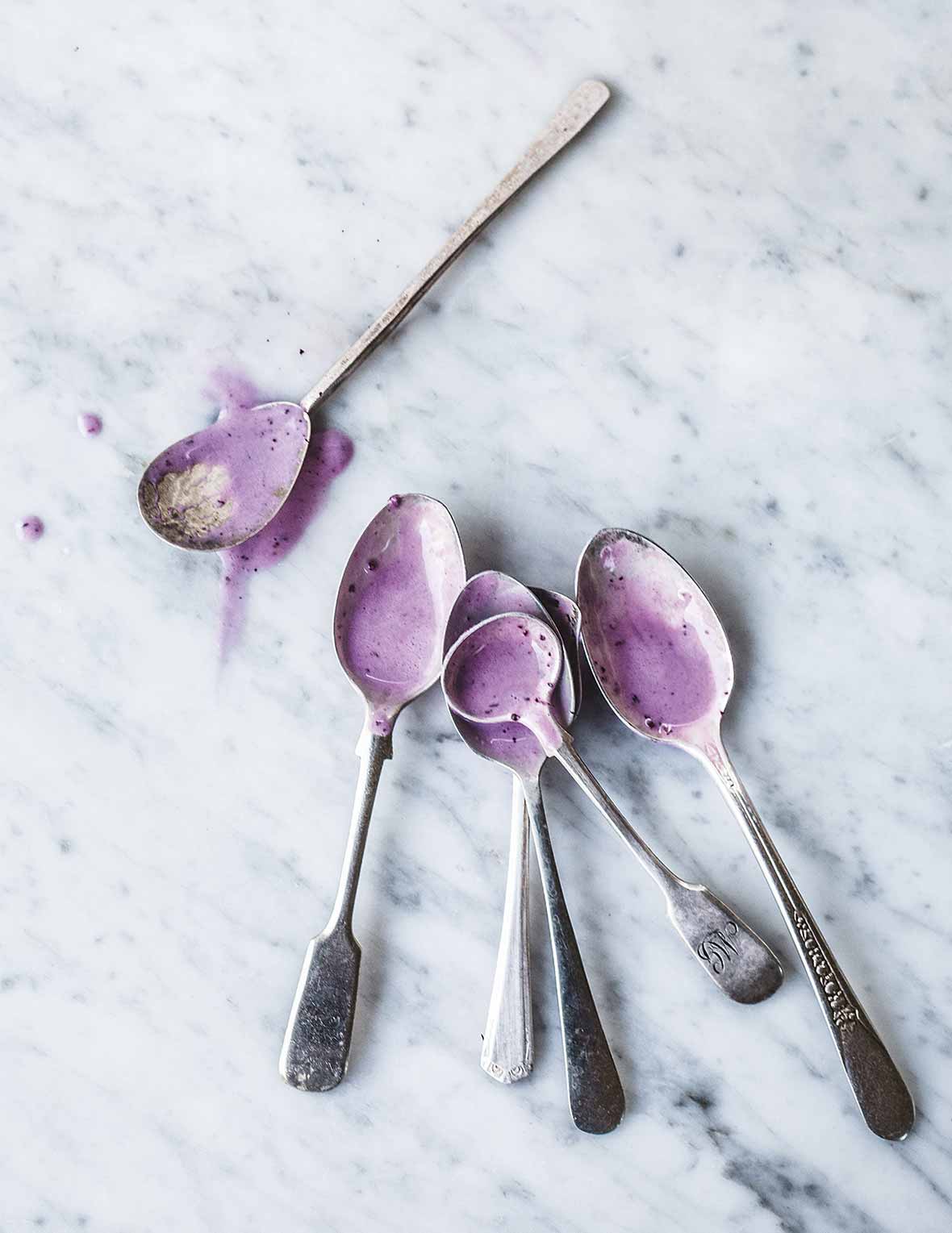 Six spoons with a little melted roasted blueberry frozen yogurt in each one.