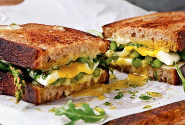 An asparagus and fried egg panini with arugula and Tallegio cheese sliced in half in parchment paper