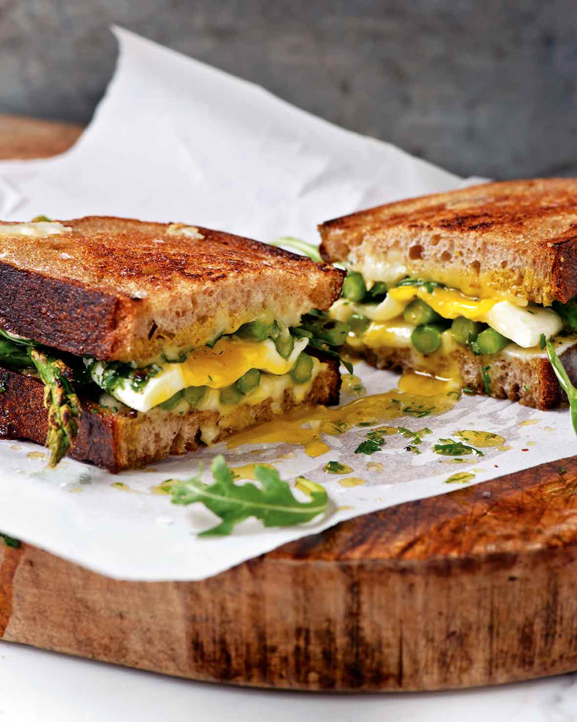 An asparagus and fried egg panini with arugula and Tallegio cheese sliced in half in parchment paper