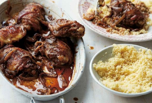 An oval dish filled with Baharat spiced chicken pieces and a bowl of couscous and plate of couscous and chicken on the side.