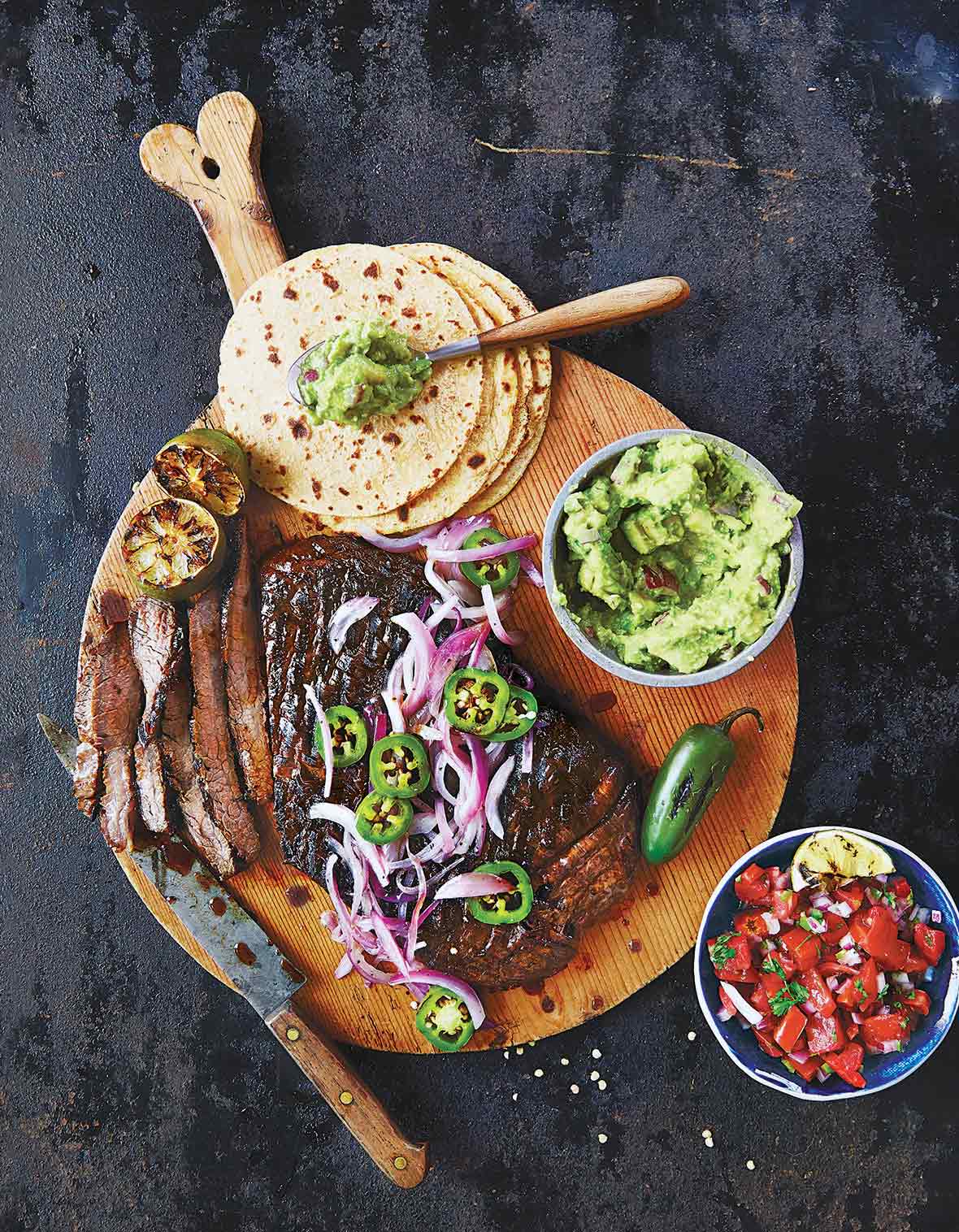 The makings of beef fajitas on a wooden board - tortillas, steak, guacamole, salsa.