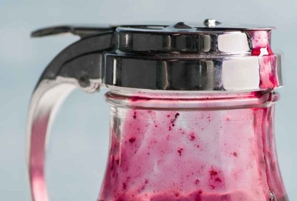 A diner-style dispenser half-filled with blueberry syrup.