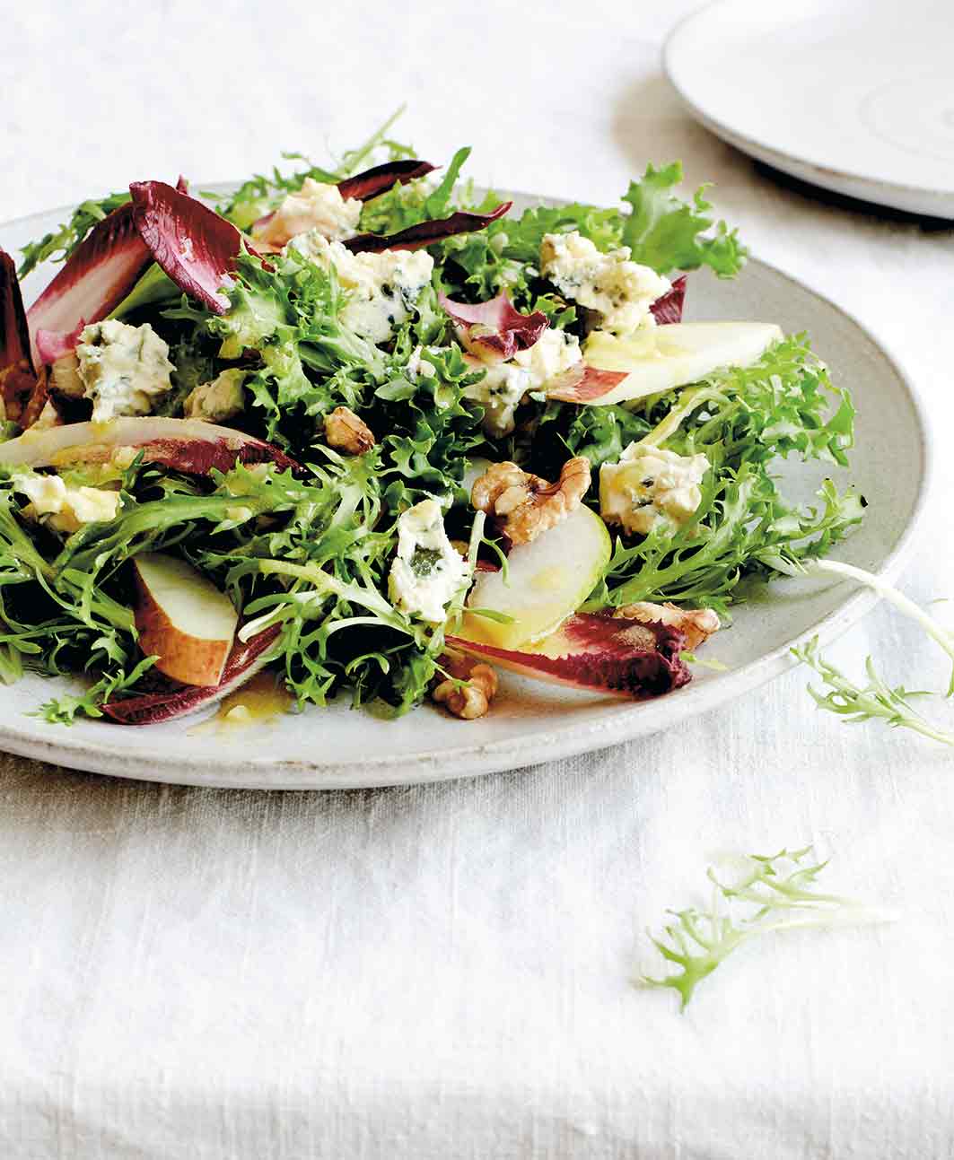 A white plate topped with endive, blue cheese, pears, and walnuts