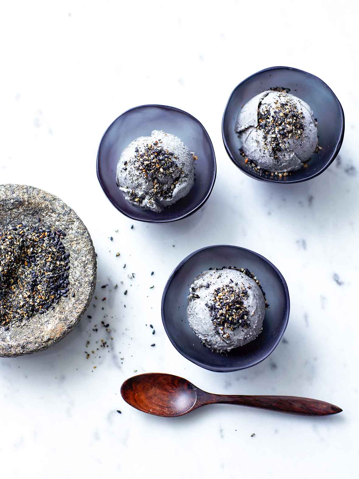 Two black bowls, each with a scoop of black sesame ice cream, sprinkled with black sesame seeds.