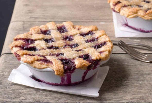 Two individual size blueberry pies on a wooden table.