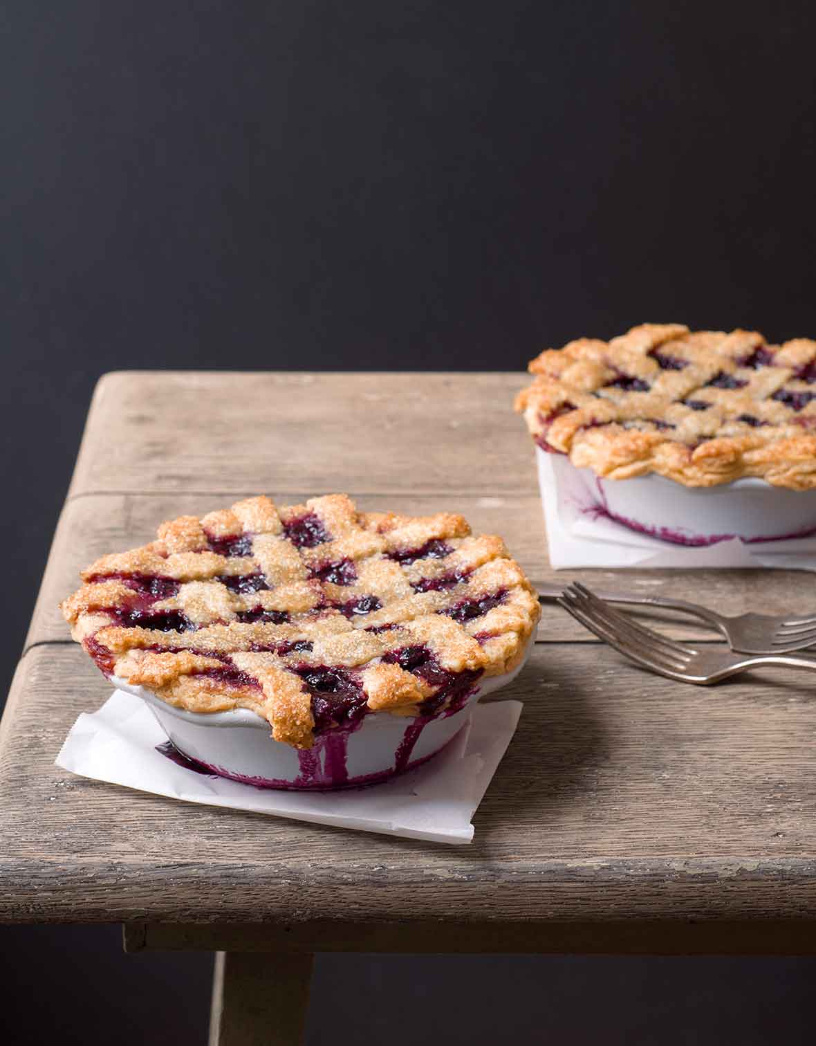 Two individual size blueberry pies on a wooden table.