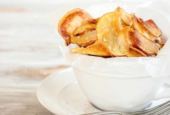 A white bowl filled with salt and vinegar potato chips with a fork resting beside.