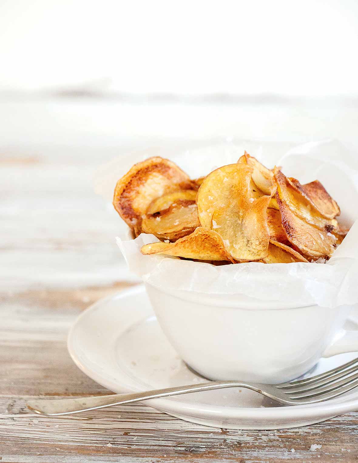 A white bowl filled with salt and vinegar potato chips with a fork resting beside.