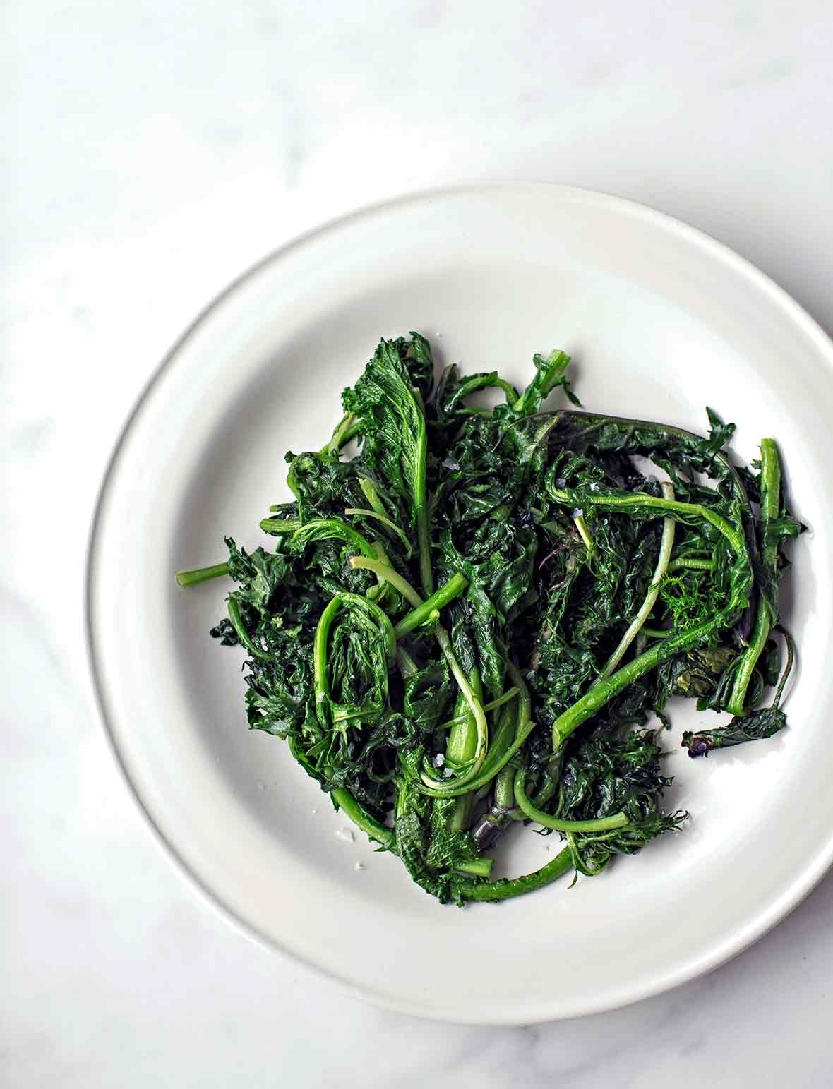 A pile of charred greens--kale and spinach--on a white plate