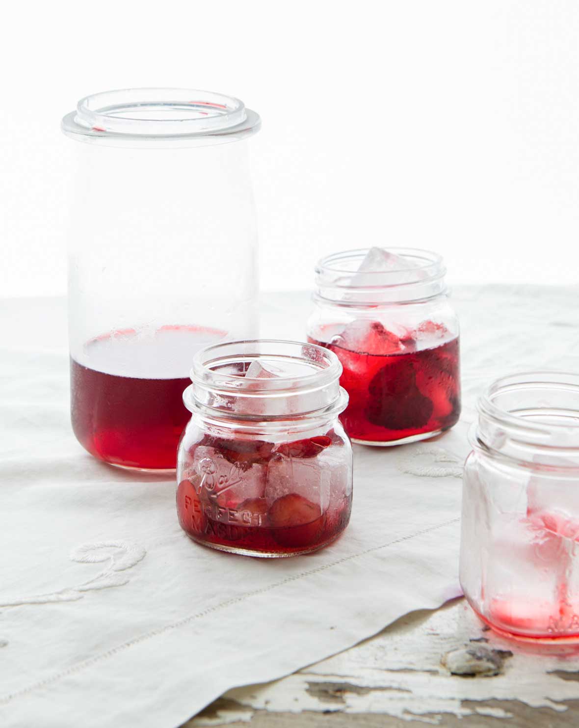 A tall bottle and several small jars filled with strawberry punch and ice cubes.
