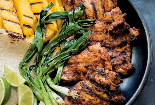 A large platter with grilled mango, chicken, scallions, tortillas, and lime, for grilled chicken tacos.
