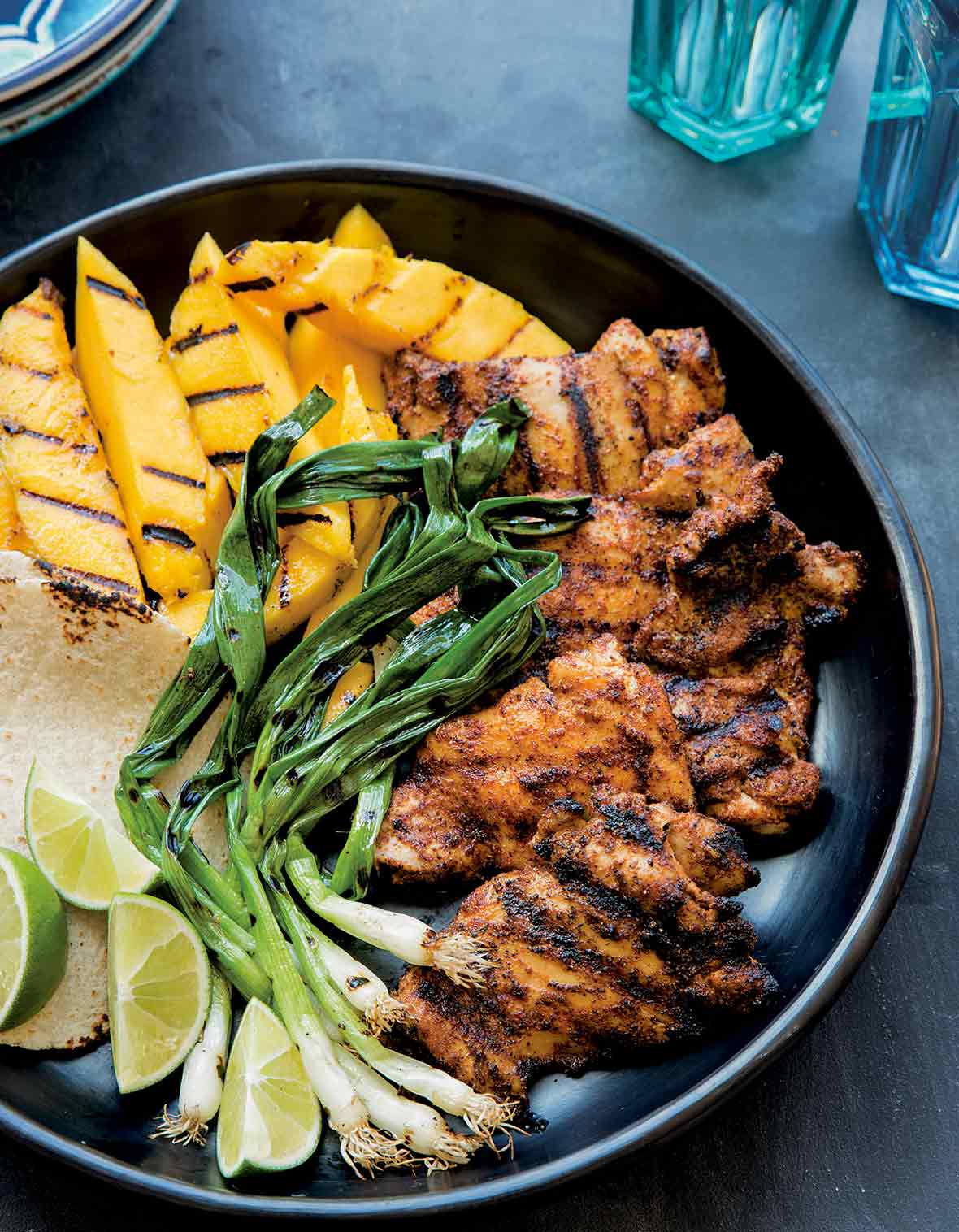 A large platter with grilled mango, chicken, scallions, tortillas, and lime, for grilled chicken tacos.
