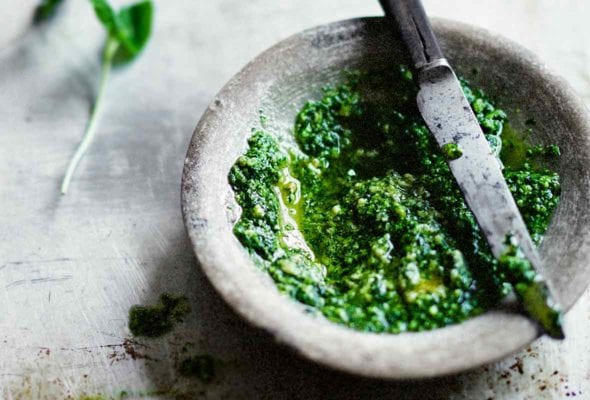 A stone bowl of mint pesto with a knife on top on a metal sheet pan