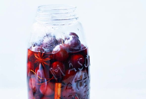 A mason jar mostly filled with pickled cherries, pickling liquid, star anise, and a cinnamon stick.