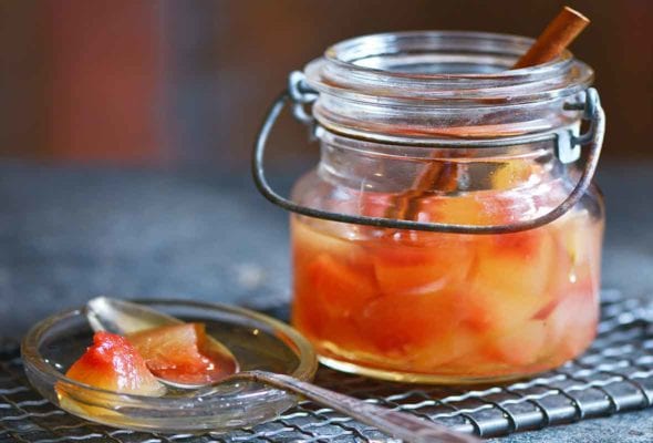 A small jar of pickled watermelon rind on a mesh rack with a spoon resting on the jar lid beside the jar.