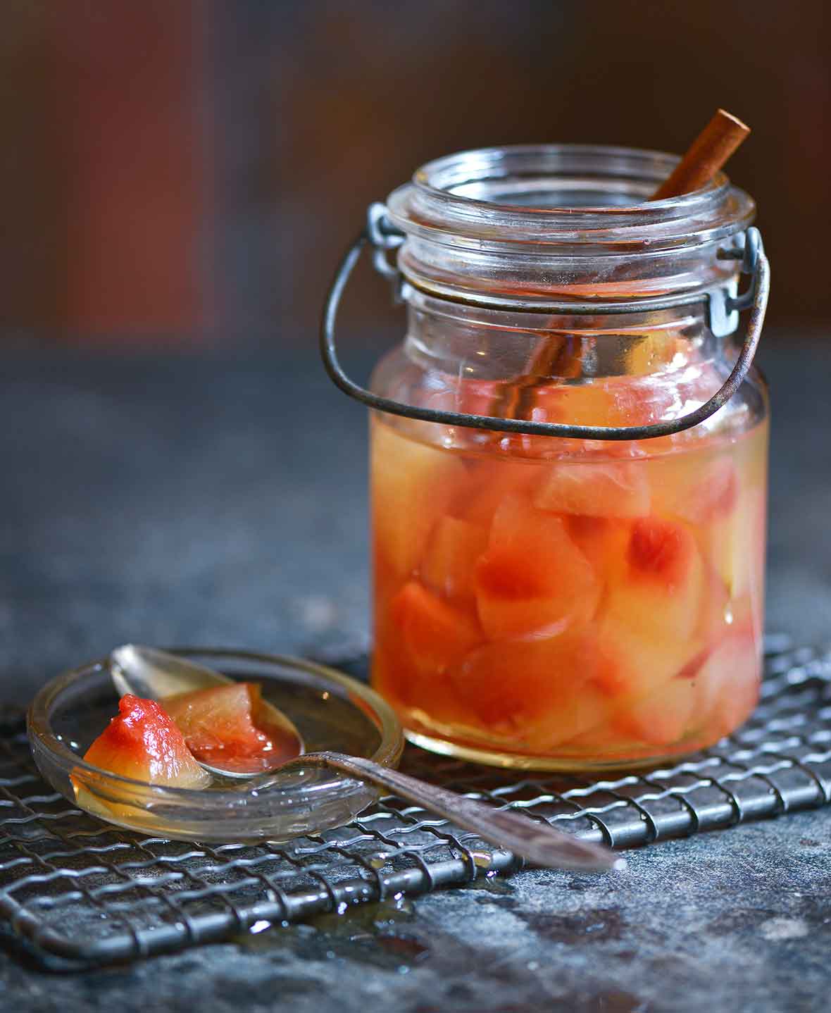 A small jar of pickled watermelon rind on a mesh rack with a spoon resting on the jar lid beside the jar.