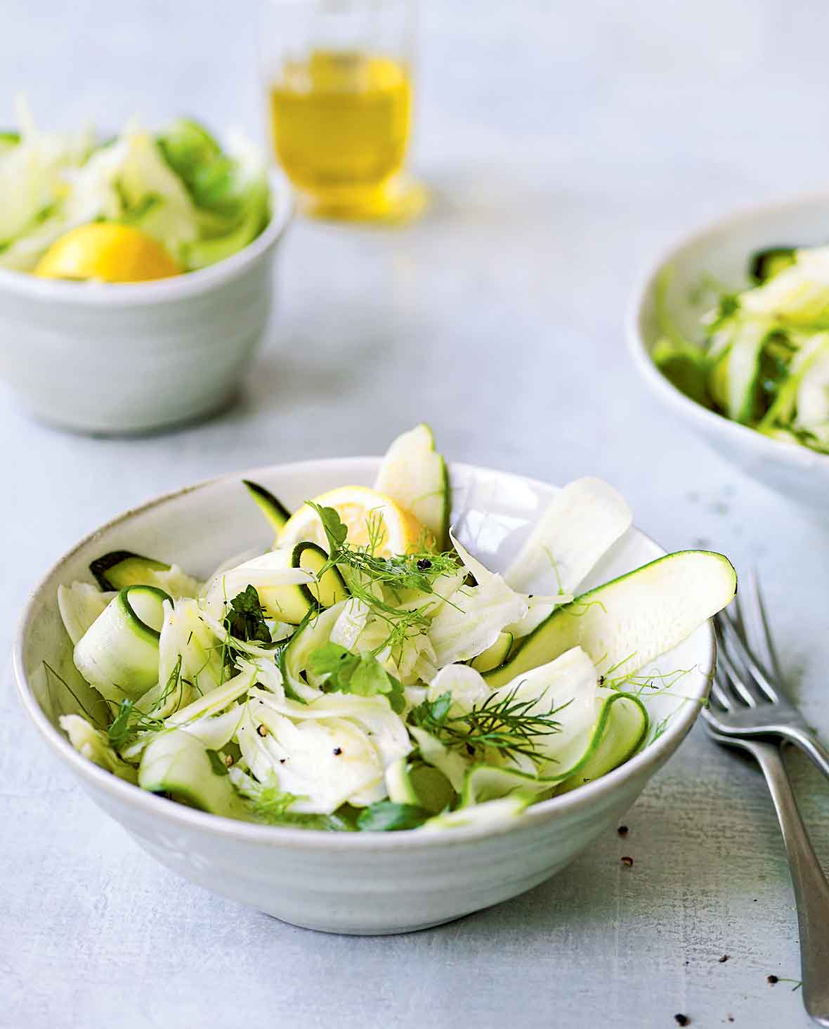 Two white bowls filled with shaved zucchini salad, topped with dill sprigs and two forks on the side.