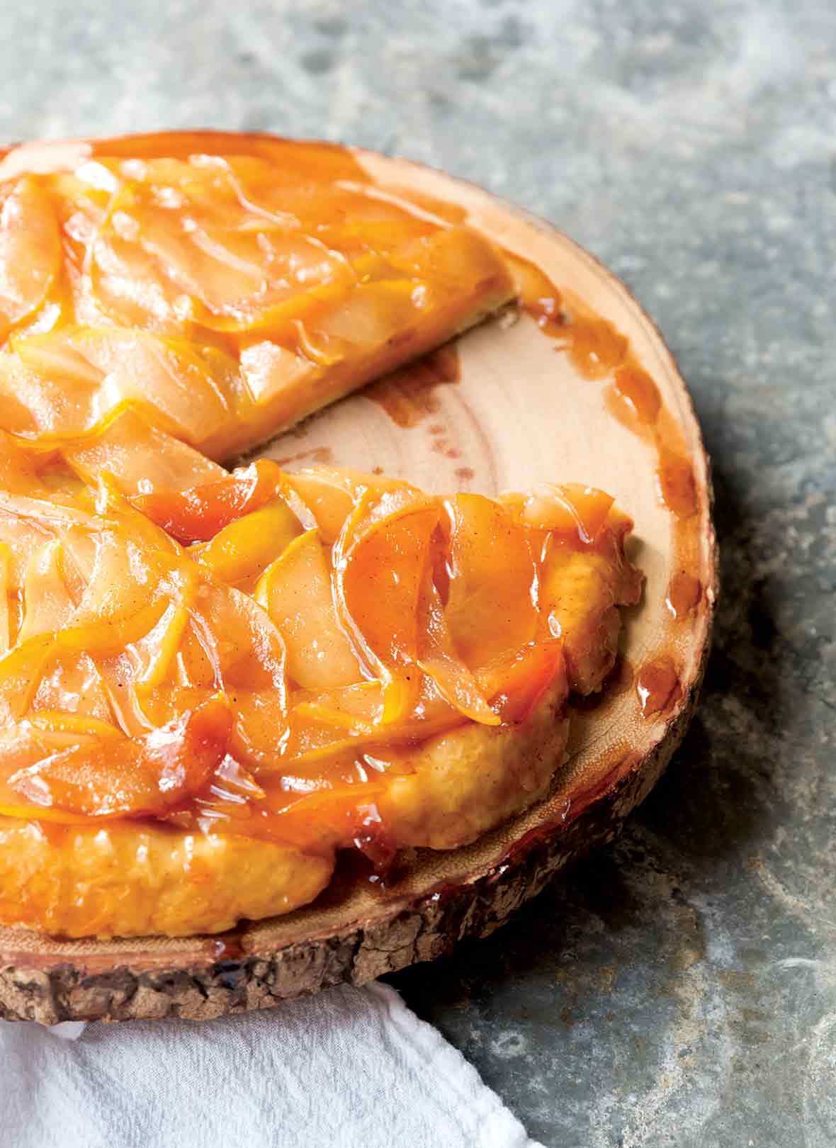 A pear tart on a wooden platter with one slice missing