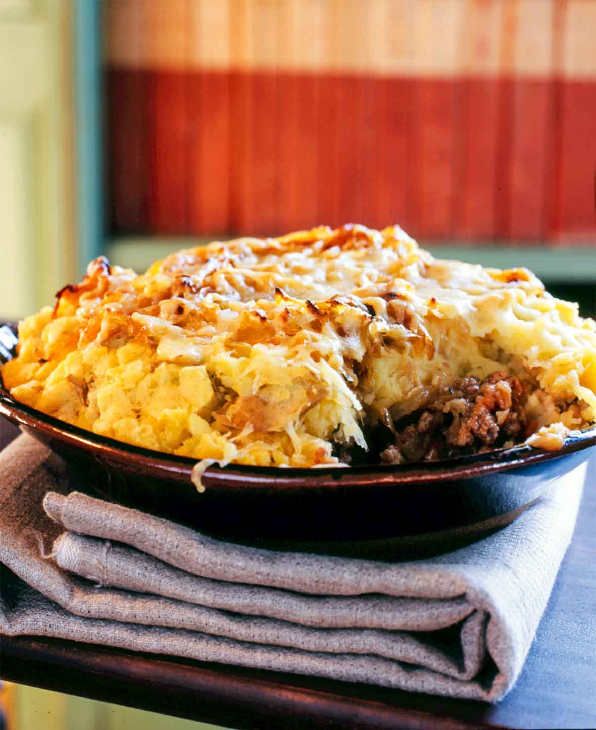 A porcelain bowl filled with shepherd's pie and topped with potatoes, onions, and cheddar