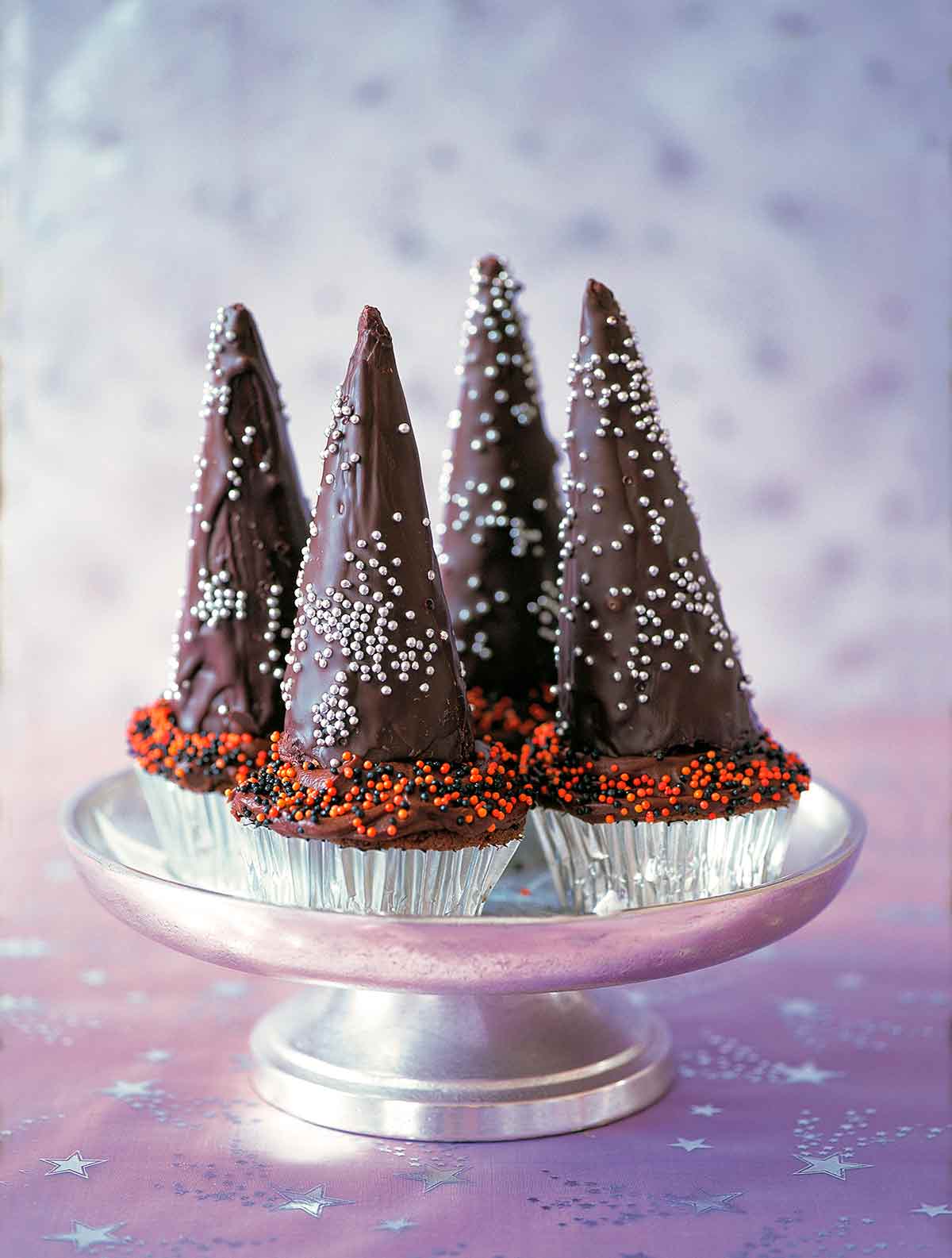 Four cupcakes with chocolate icing, topped with chocolate wizard hats.