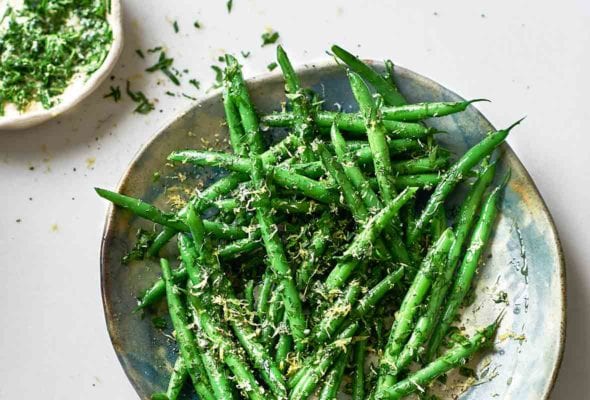 A serving platter piled with green beans and sprinkled with gremolata. A small dish of gremolata sits beside the serving plate.