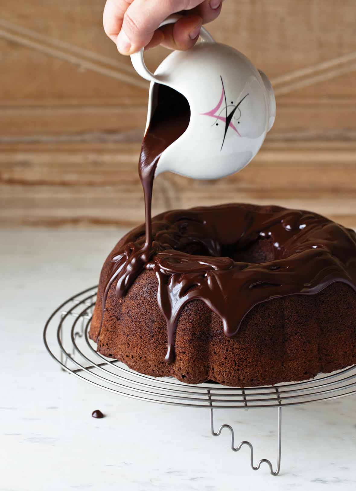Chocolate ganache being poured over a chocolate Bundt cake that is on a wire stand