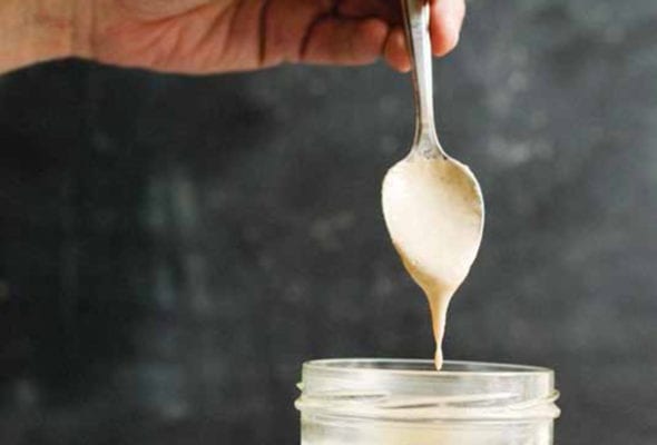 A canning jar mostly filled with creamy dressing. A spoon is held above the jar with dressing dripping off.