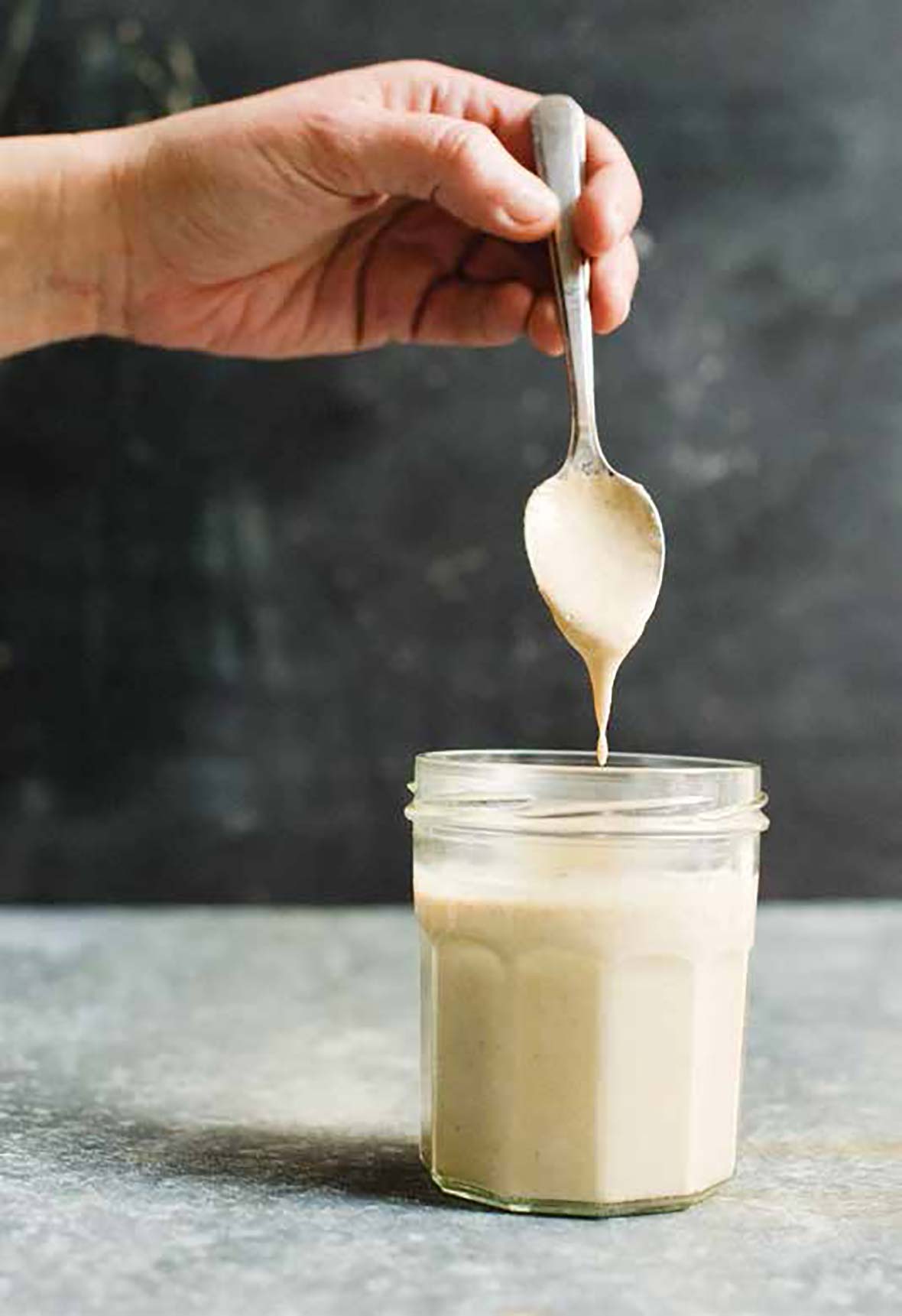 A canning jar mostly filled with creamy dressing. A spoon is held above the jar with dressing dripping off.