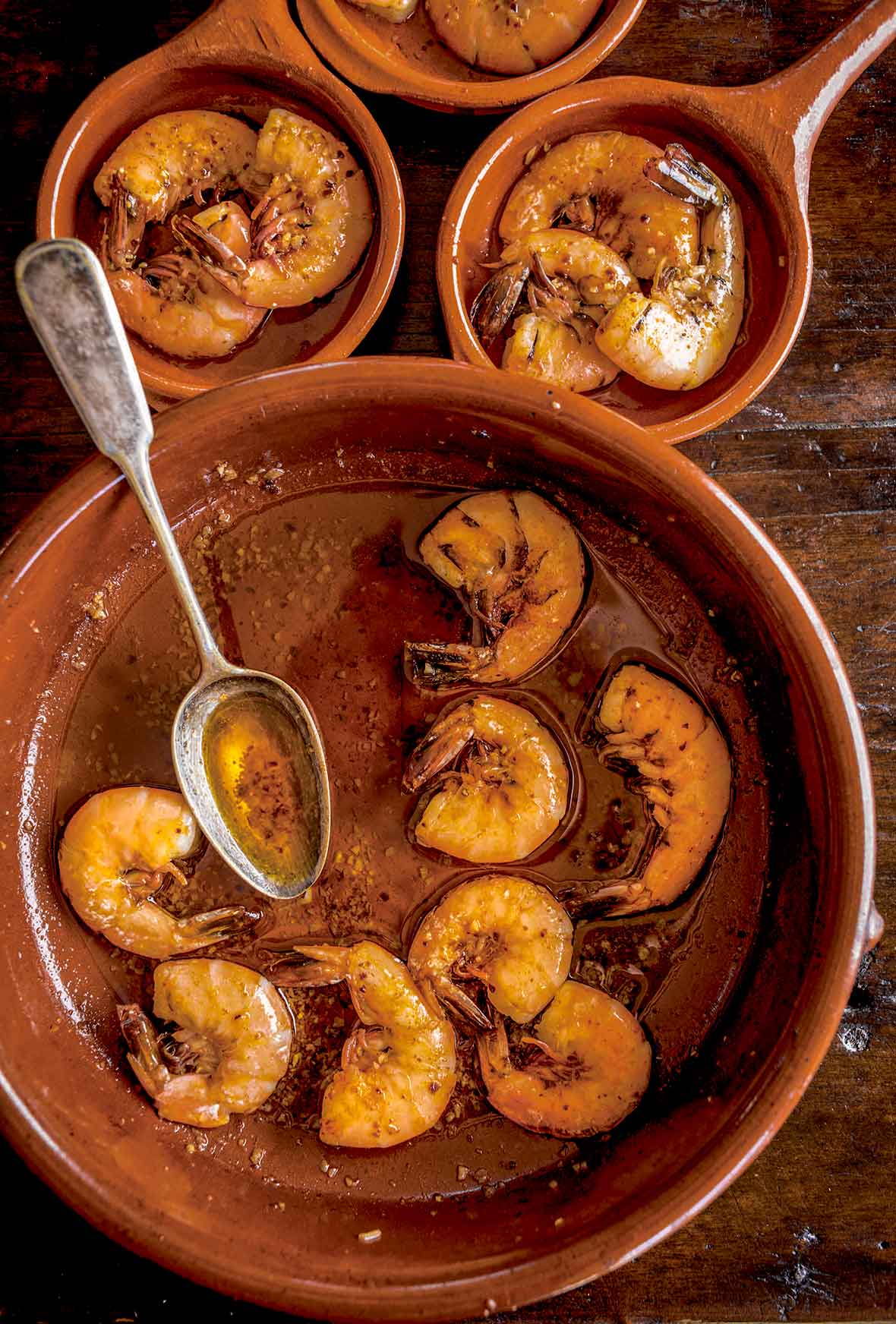 Three crockery bowls filled with cooked shrimp with smoked paprika oil