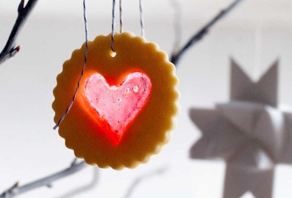 A scalloped round sugar cookie with a heart-shaped windowpane cutout hanging form a tree branch