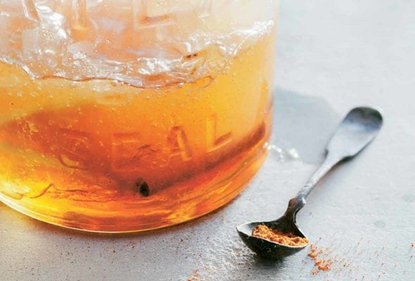 Glass jar with a cold and flu drink with a cinnamon stick, a spoon with ginger
