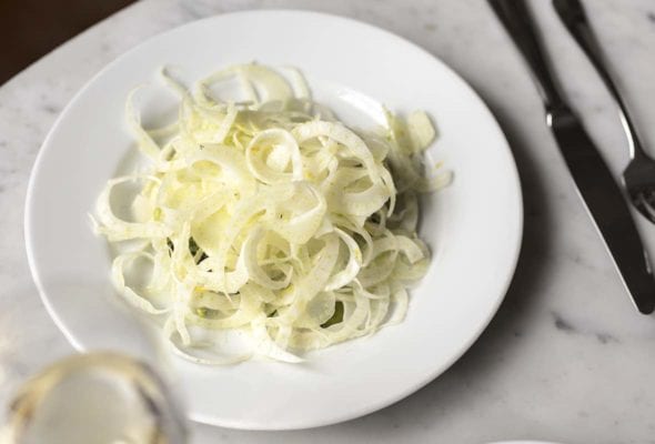 White plate of shaved fennel salad with olives, and provolone cheese