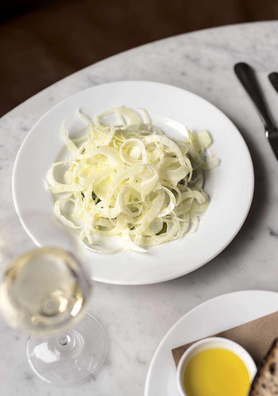 White plate of shaved fennel salad with provolone cheese, and a glass of wine