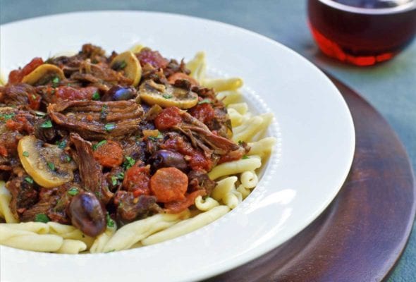 A white bowl filled with French beef stew piled atop pasta.