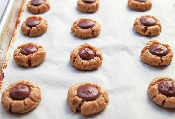A parchment lined baking sheet filled with rows of round peanut butter cookies with chocolate centers.