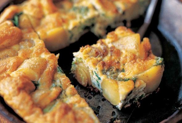 Cast iron skillet of broccolini and potato frittata, with a wedge on a metal spatula