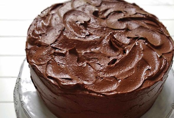 A Hershey chocolate cake with swirled chocolate frosting on a white cake stand
