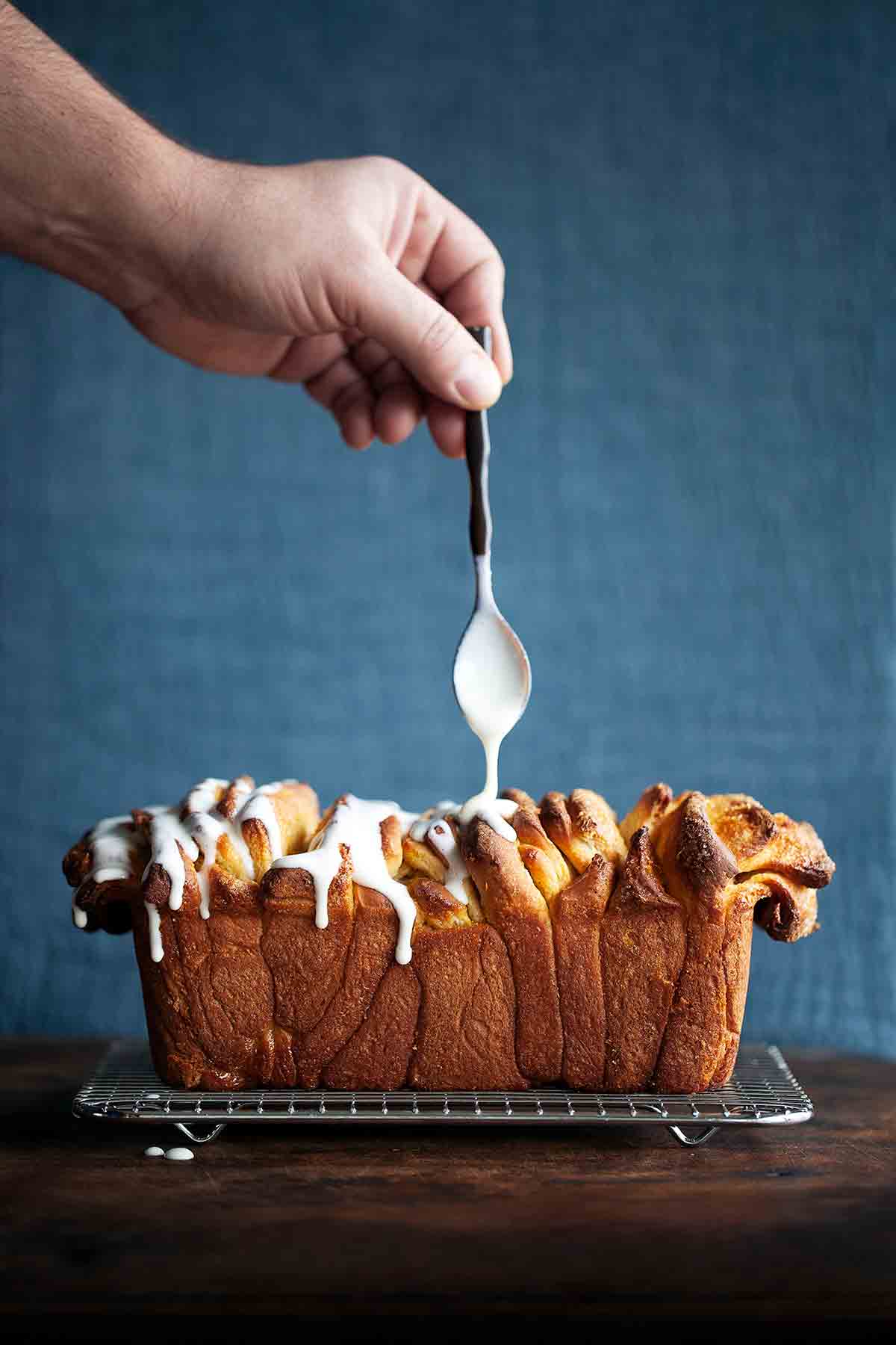 A person glazing a lemon pull-apart coffee cake on a wire rack.