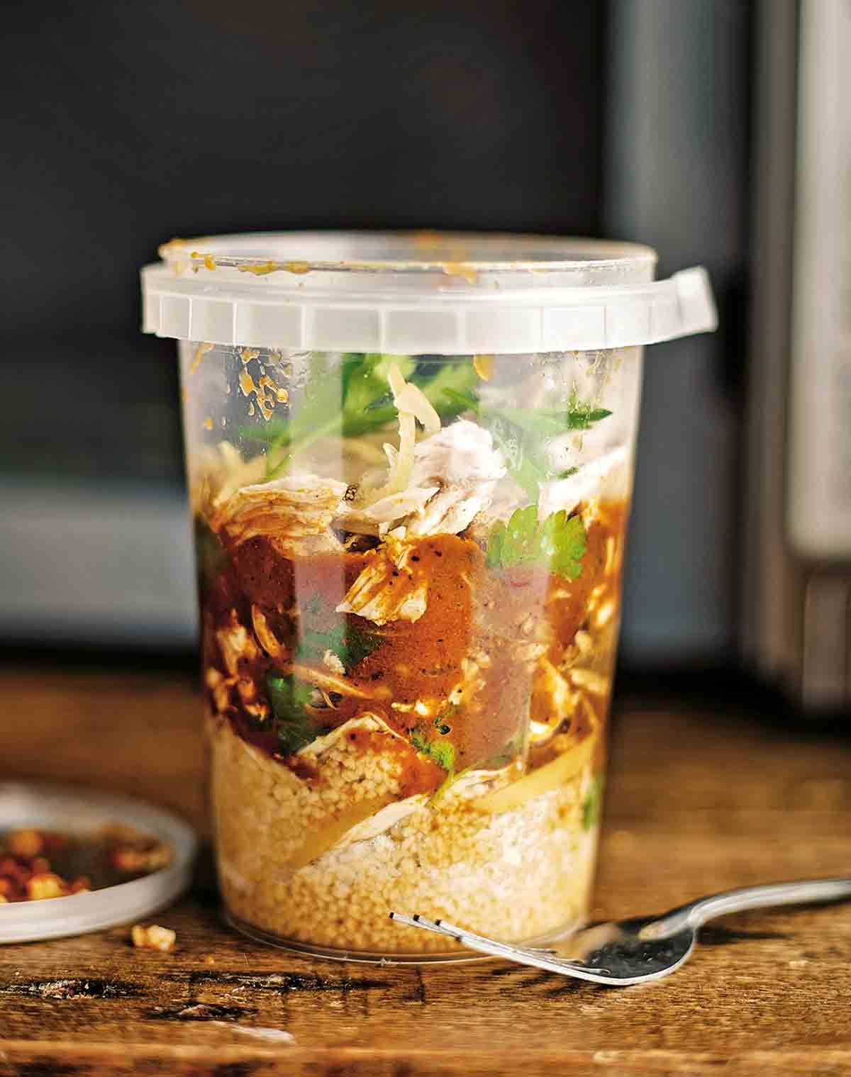 Plastic container or North African chicken soup with shredded chicken, ras el hanout, couscous, and preserved lemon