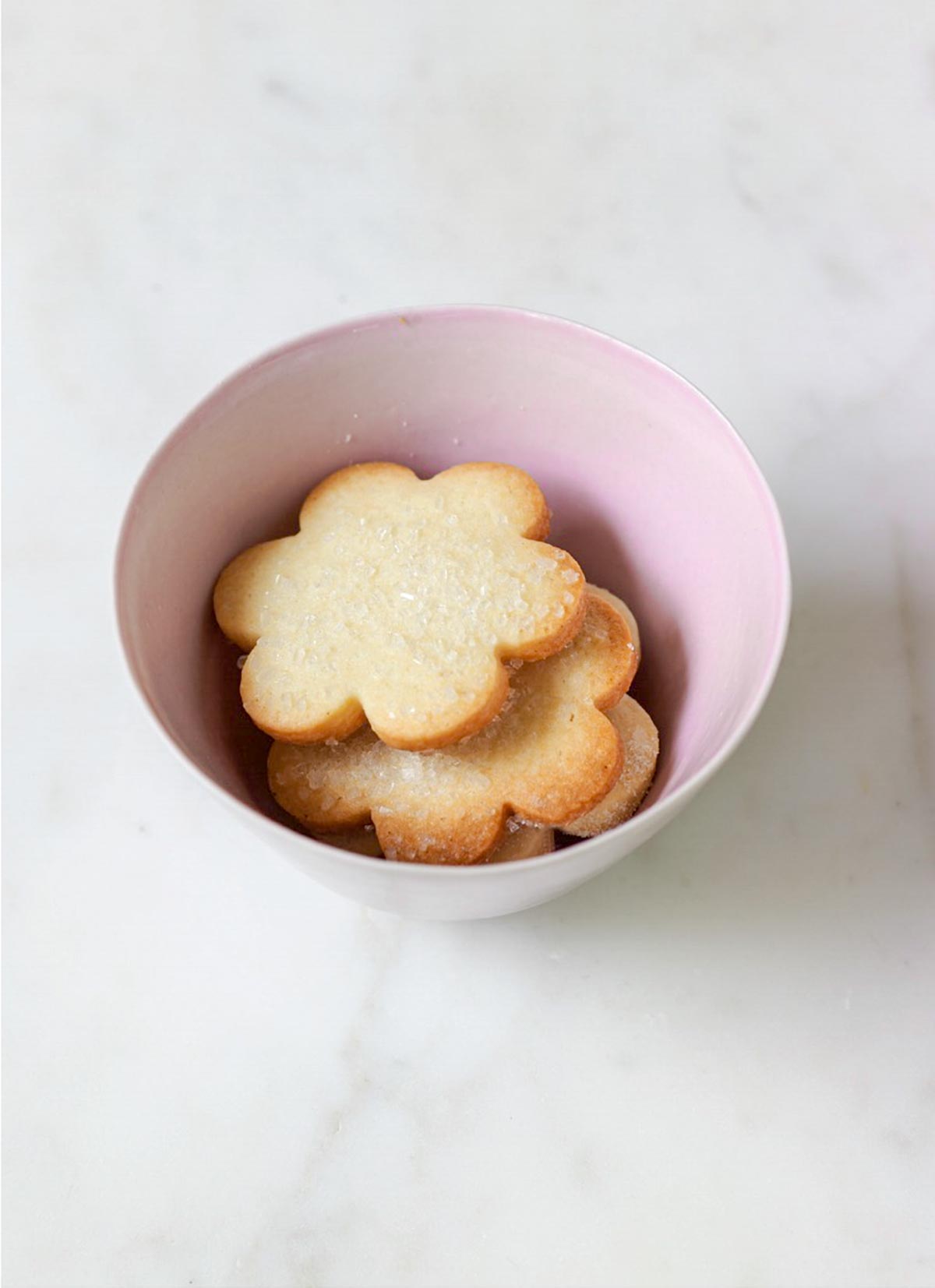 A pink bowl filled with flower-shaped sugar cookies topped with decorating sugar