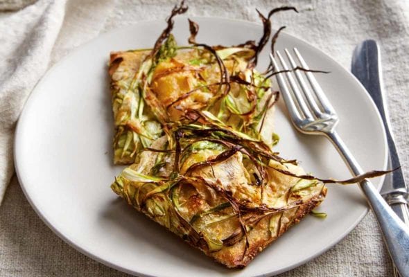 Plate with shaved asparagus pizza, fork and knife, on a kitchen towel